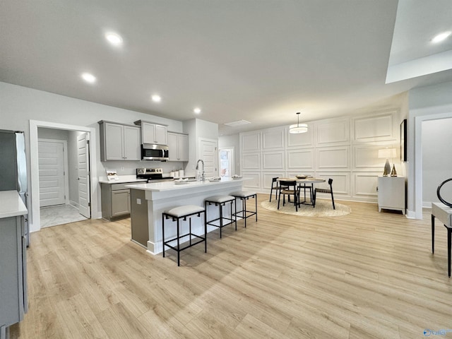 kitchen featuring gray cabinets, a sink, a kitchen breakfast bar, stainless steel appliances, and light countertops