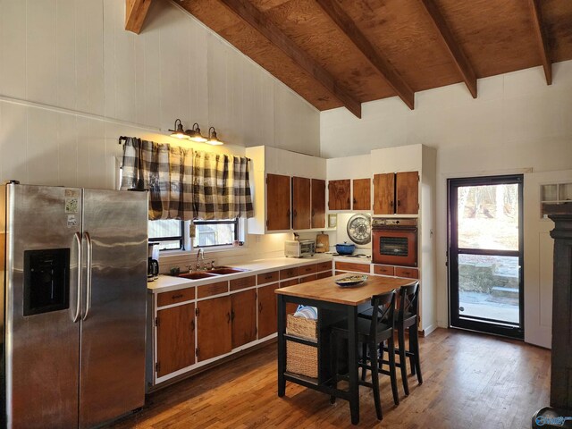 kitchen with black oven, a healthy amount of sunlight, stainless steel refrigerator with ice dispenser, and vaulted ceiling with beams