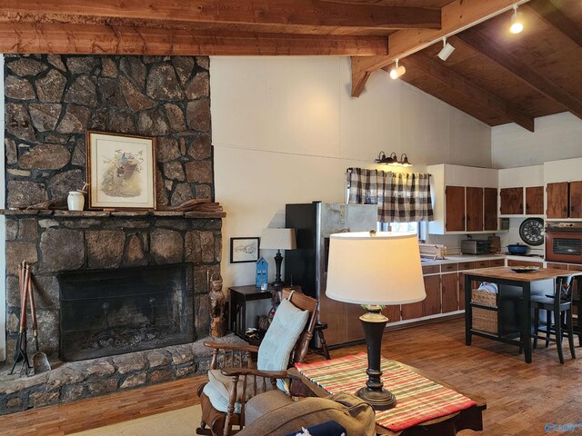 living room with beam ceiling, wooden ceiling, a stone fireplace, high vaulted ceiling, and light hardwood / wood-style floors