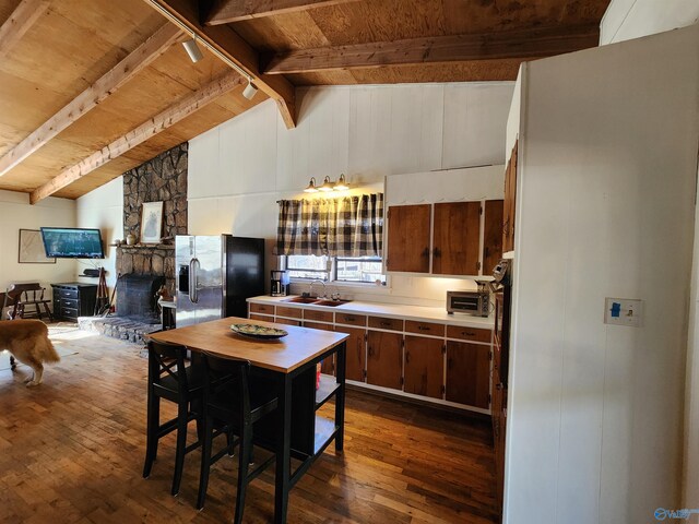 kitchen with sink, a stone fireplace, lofted ceiling with beams, dark hardwood / wood-style floors, and stainless steel fridge