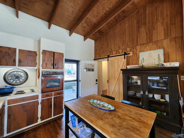 kitchen featuring oven, wooden walls, dark hardwood / wood-style floors, a barn door, and beam ceiling