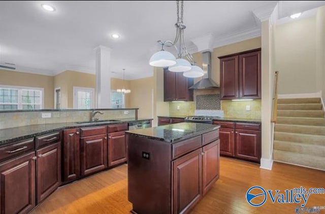 kitchen with sink, wall chimney exhaust hood, a kitchen island, a notable chandelier, and light hardwood / wood-style floors