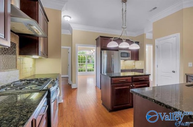 kitchen featuring appliances with stainless steel finishes, light wood-type flooring, backsplash, wall chimney range hood, and hanging light fixtures