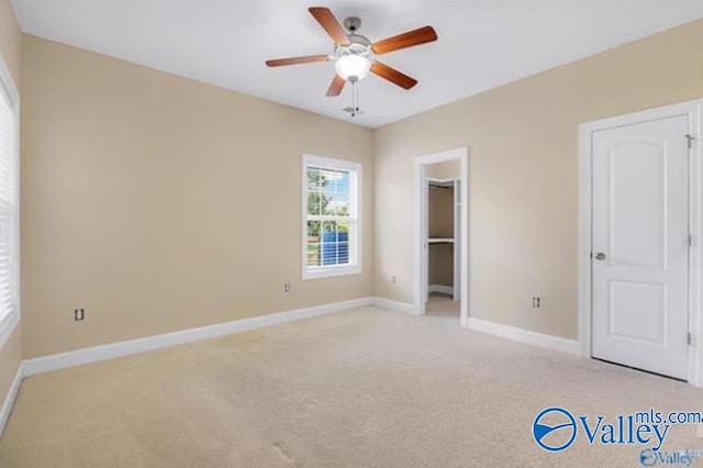 unfurnished bedroom with ceiling fan, a spacious closet, light carpet, and a closet