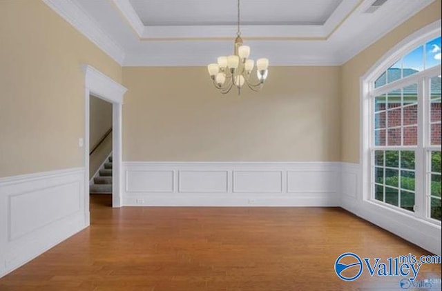 unfurnished dining area featuring wood-type flooring, a raised ceiling, ornamental molding, and a notable chandelier