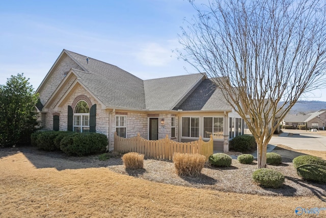 view of front of house with stone siding, a shingled roof, and fence