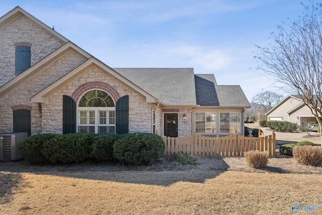 view of front of house with cooling unit, stone siding, roof with shingles, and fence