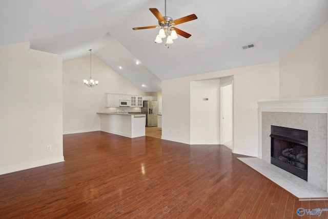 unfurnished living room featuring visible vents, wood finished floors, a tile fireplace, baseboards, and ceiling fan with notable chandelier