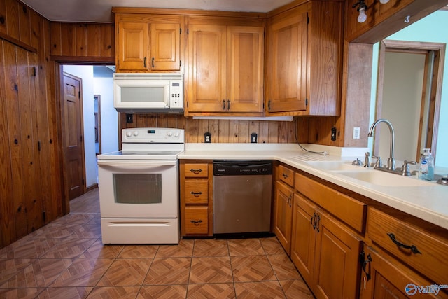 kitchen featuring wood walls, light countertops, brown cabinets, white appliances, and a sink