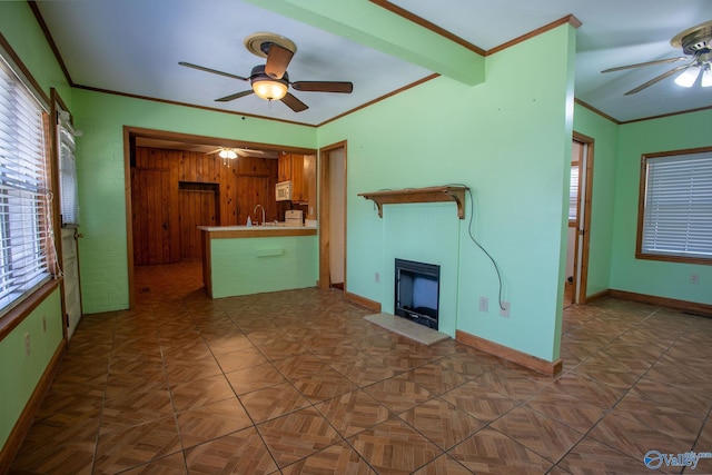 unfurnished living room featuring a ceiling fan, a sink, a fireplace, crown molding, and baseboards