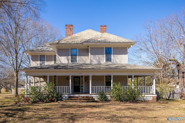 country-style home with covered porch, a chimney, and a front yard