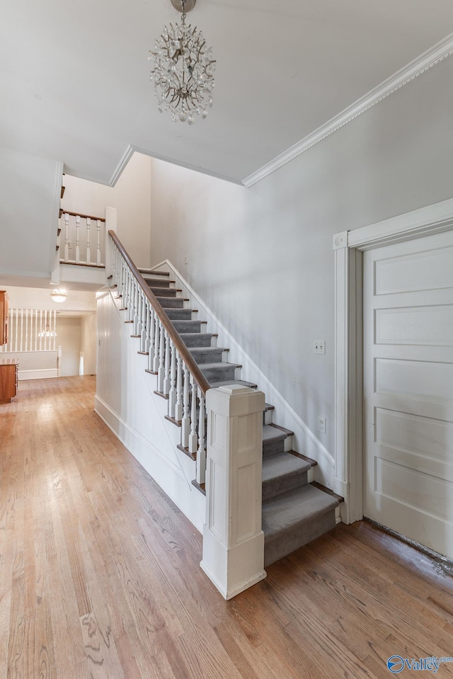 stairway featuring an inviting chandelier, wood finished floors, and ornamental molding