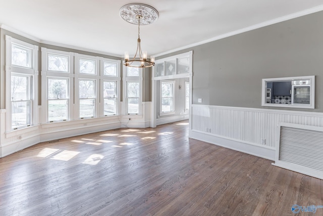 unfurnished dining area featuring wood finished floors, a wainscoted wall, visible vents, an inviting chandelier, and crown molding