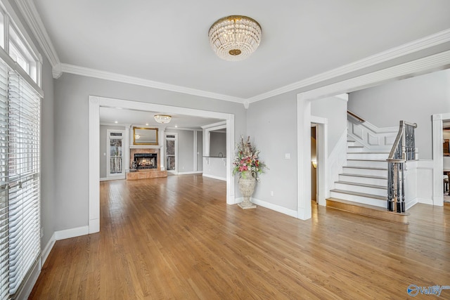 unfurnished living room featuring crown molding, wood-type flooring, a fireplace, and a chandelier