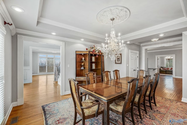 dining space with a raised ceiling, ornamental molding, an inviting chandelier, and light hardwood / wood-style floors