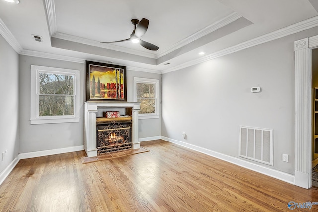 unfurnished living room featuring wood-type flooring, ornamental molding, ceiling fan, and a tray ceiling