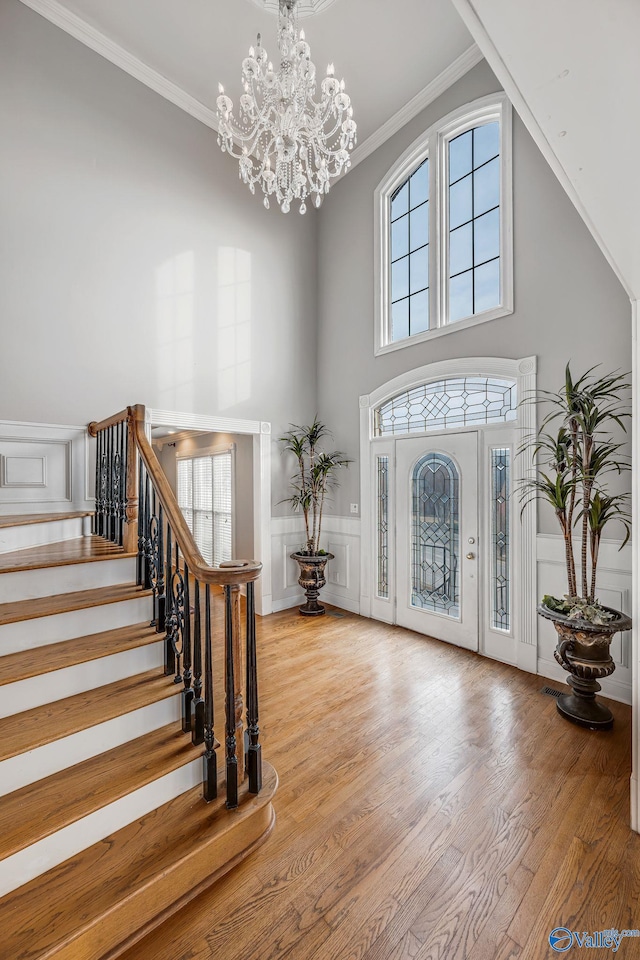 foyer entrance featuring crown molding, a towering ceiling, a chandelier, and light hardwood / wood-style floors