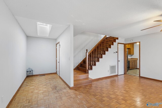 interior space featuring ceiling fan, a skylight, a textured ceiling, and light parquet floors