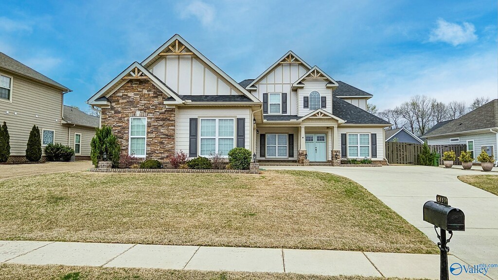 craftsman house featuring concrete driveway, fence, stone siding, board and batten siding, and a front yard