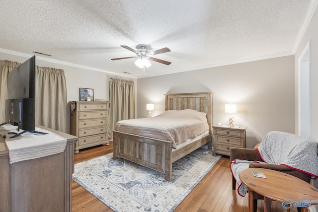 bedroom featuring ceiling fan, a textured ceiling, light wood-style flooring, visible vents, and crown molding