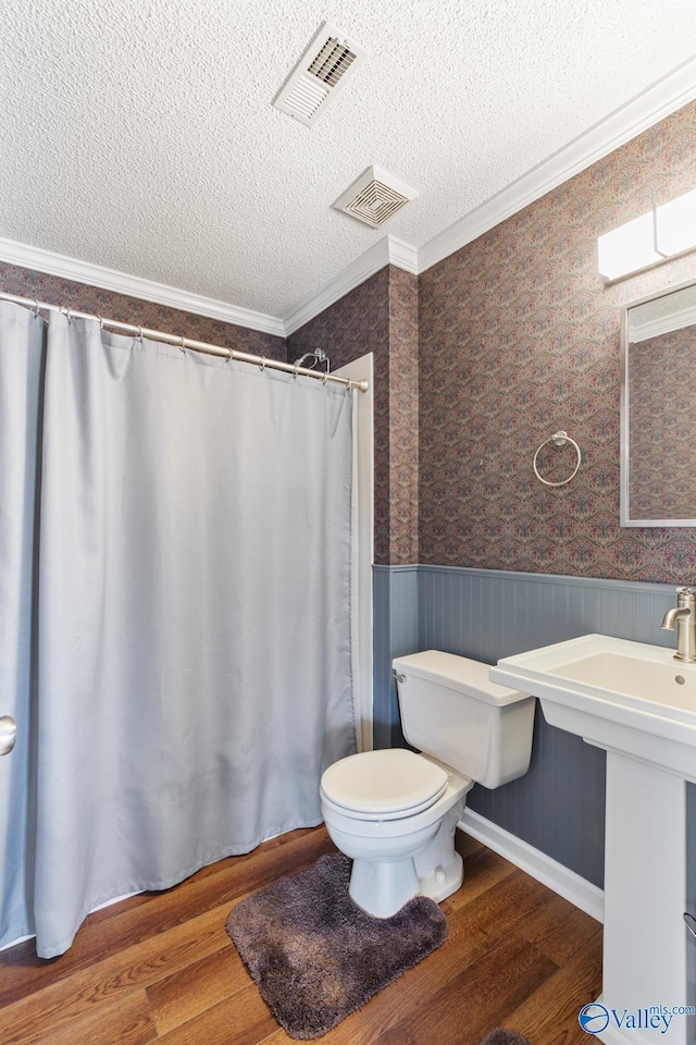 bathroom with a wainscoted wall, visible vents, a textured ceiling, and wood finished floors