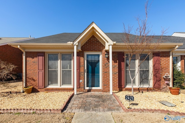 ranch-style house featuring roof with shingles and brick siding