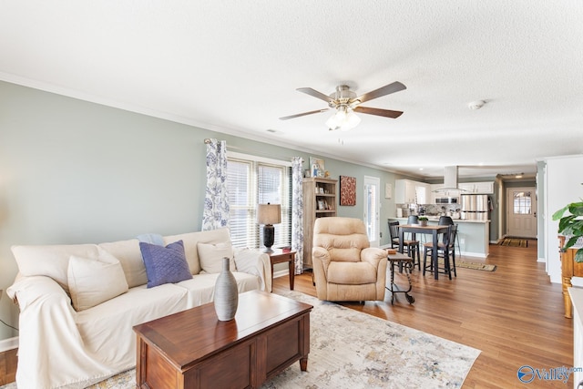 living area featuring plenty of natural light, light wood-style flooring, ornamental molding, and a textured ceiling