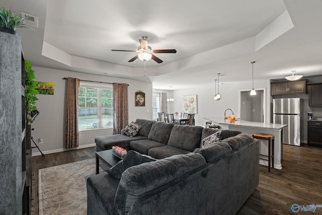 living room with a tray ceiling, ceiling fan, sink, and dark hardwood / wood-style flooring