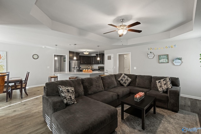 living room with a raised ceiling, dark hardwood / wood-style flooring, ceiling fan, and sink