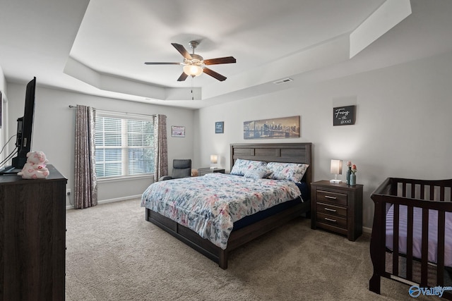 carpeted bedroom with ceiling fan and a raised ceiling