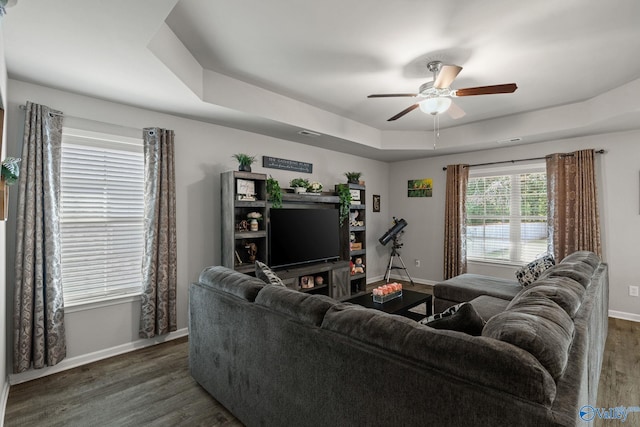 living room featuring a tray ceiling, ceiling fan, and dark wood-type flooring