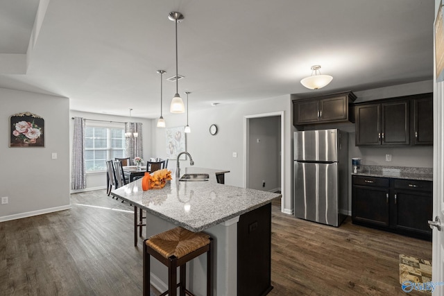 kitchen featuring stainless steel fridge, a breakfast bar, light stone countertops, a center island with sink, and sink