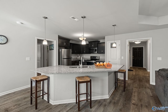 kitchen with dark wood-type flooring, stainless steel appliances, a kitchen bar, decorative light fixtures, and sink