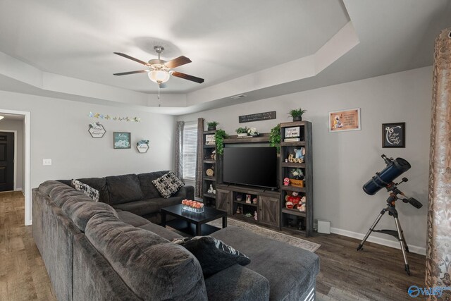 living room with ceiling fan, a raised ceiling, and dark hardwood / wood-style floors