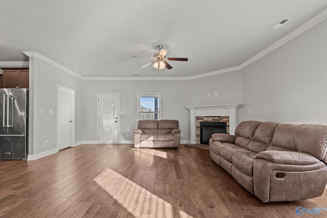 living room with a stone fireplace, wood-type flooring, ornamental molding, and ceiling fan