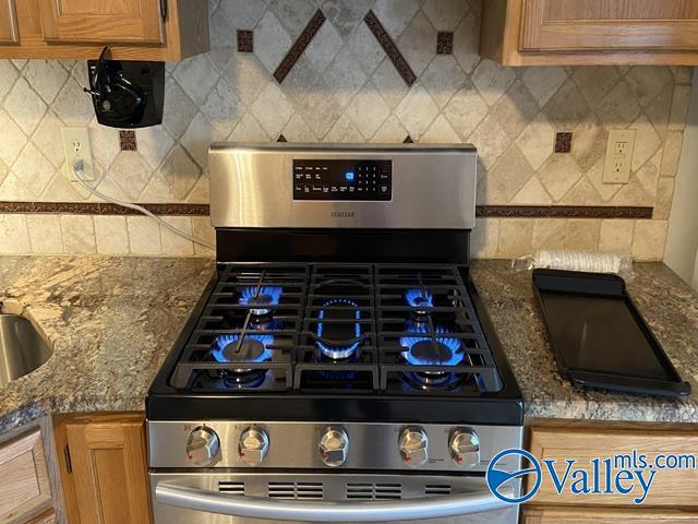 kitchen featuring tasteful backsplash, stainless steel gas range oven, and dark stone counters