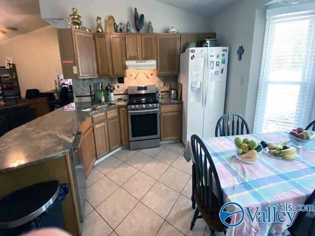 kitchen featuring stainless steel appliances, vaulted ceiling, tasteful backsplash, and light tile patterned flooring