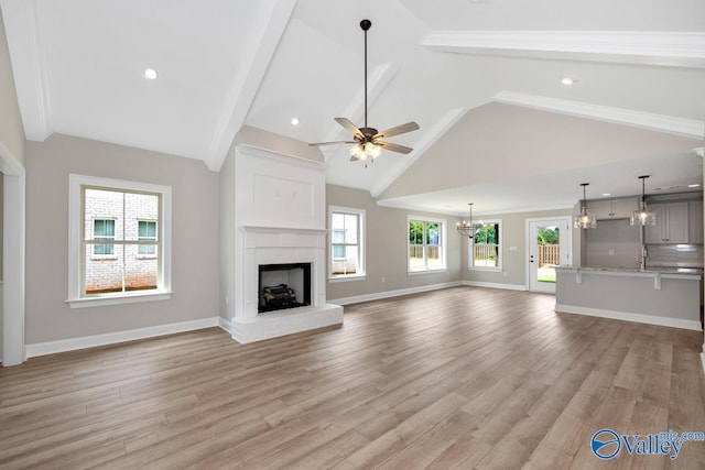 unfurnished living room with ceiling fan with notable chandelier, high vaulted ceiling, a fireplace, and light hardwood / wood-style floors