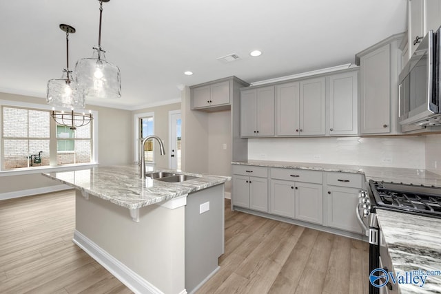 kitchen with sink, hanging light fixtures, stainless steel appliances, ornamental molding, and an island with sink