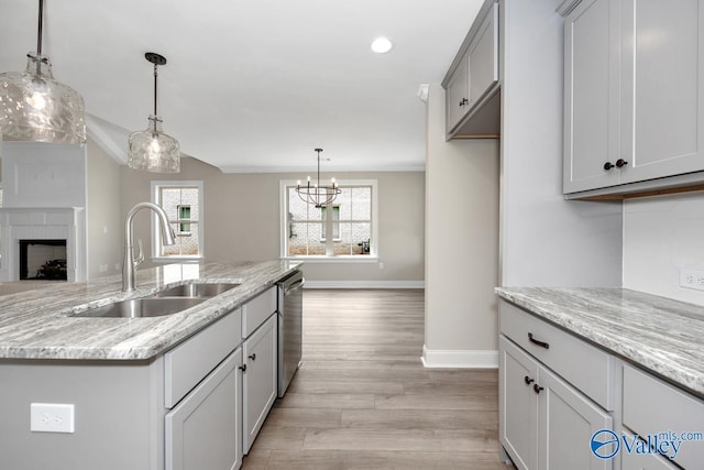 kitchen featuring sink, stainless steel dishwasher, an island with sink, and light stone countertops