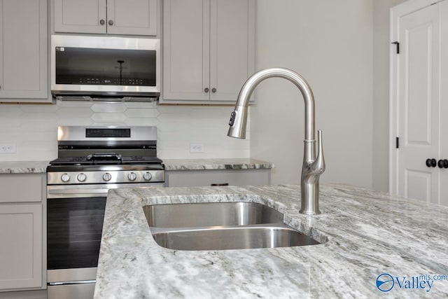 kitchen with sink, backsplash, stainless steel appliances, and light stone countertops