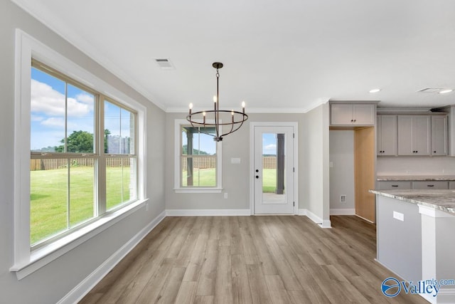 unfurnished dining area with ornamental molding, a chandelier, and light wood-type flooring