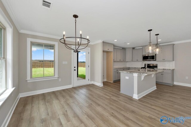 kitchen with pendant lighting, appliances with stainless steel finishes, gray cabinetry, a kitchen island with sink, and light stone counters