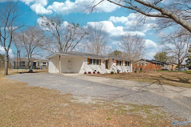 ranch-style home featuring a front lawn, a trampoline, gravel driveway, and an attached carport