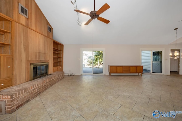 unfurnished living room featuring a brick fireplace, built in shelves, ceiling fan, high vaulted ceiling, and wood walls