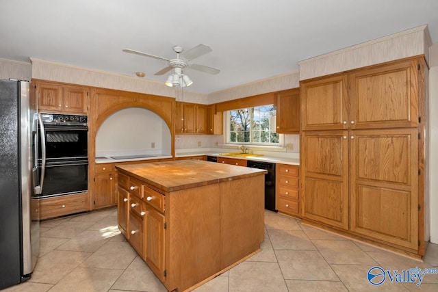 kitchen with a center island, black appliances, sink, ceiling fan, and butcher block countertops