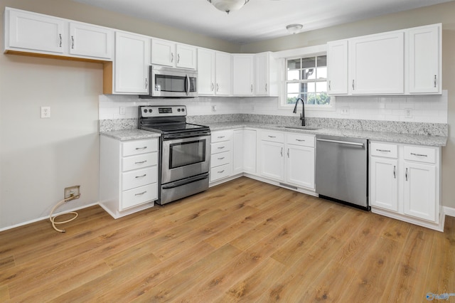 kitchen with stainless steel appliances, white cabinetry, light hardwood / wood-style floors, and sink