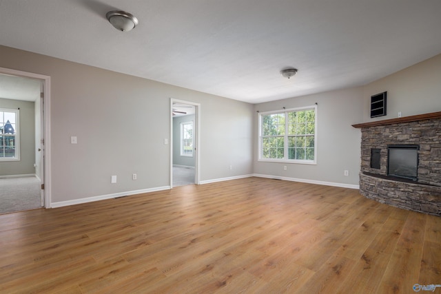 unfurnished living room featuring light wood-type flooring, a stone fireplace, and plenty of natural light