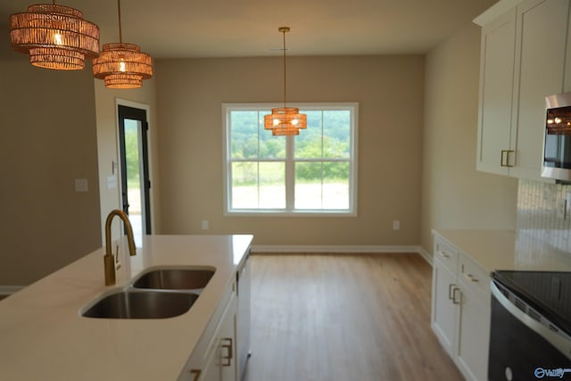 kitchen featuring an inviting chandelier, light wood-style flooring, stainless steel microwave, light countertops, and a sink