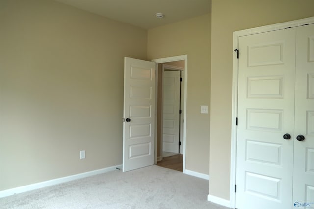unfurnished bedroom with a closet, light carpet, and baseboards
